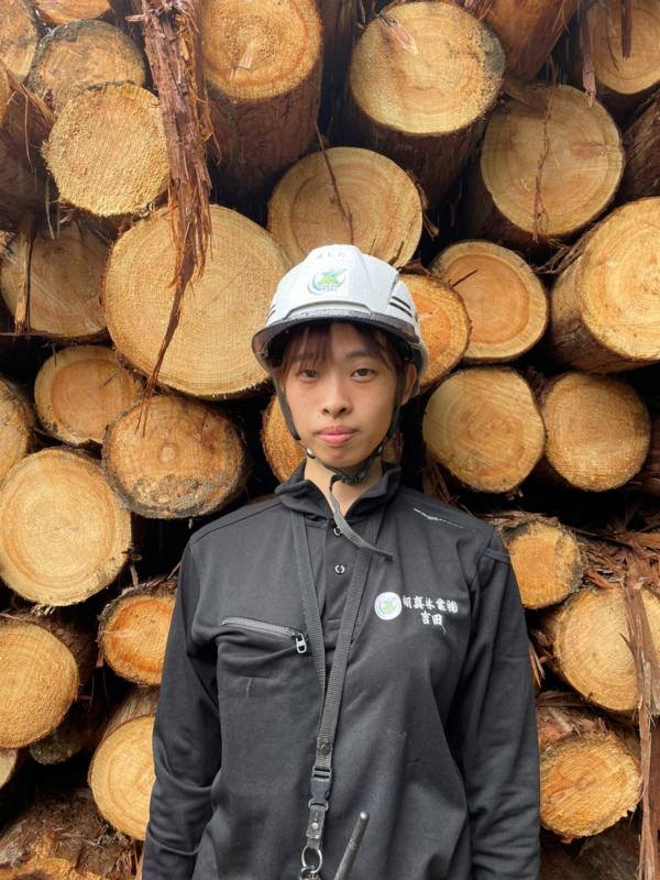 自分の背よりも高く積まれる丸太の前に立つ吉田さん